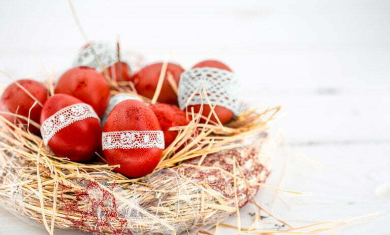 Red Easter eggs in a nest of hay, tied a lace ribbon, close-up , lying on a white wooden background still life
